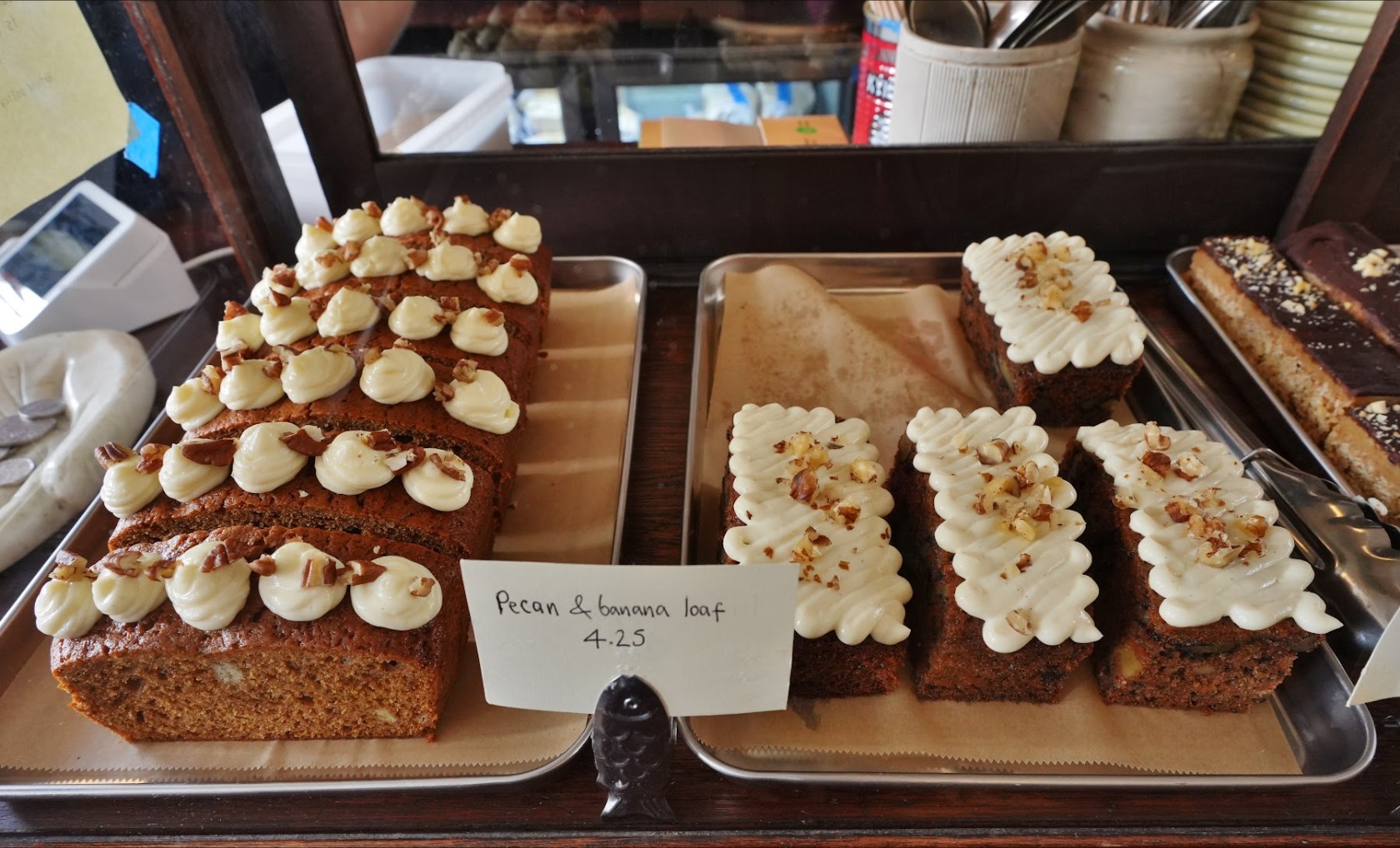 The cake cabinet: traybakes with piped cream, and a handwritten label for the pecan and banana loaf.