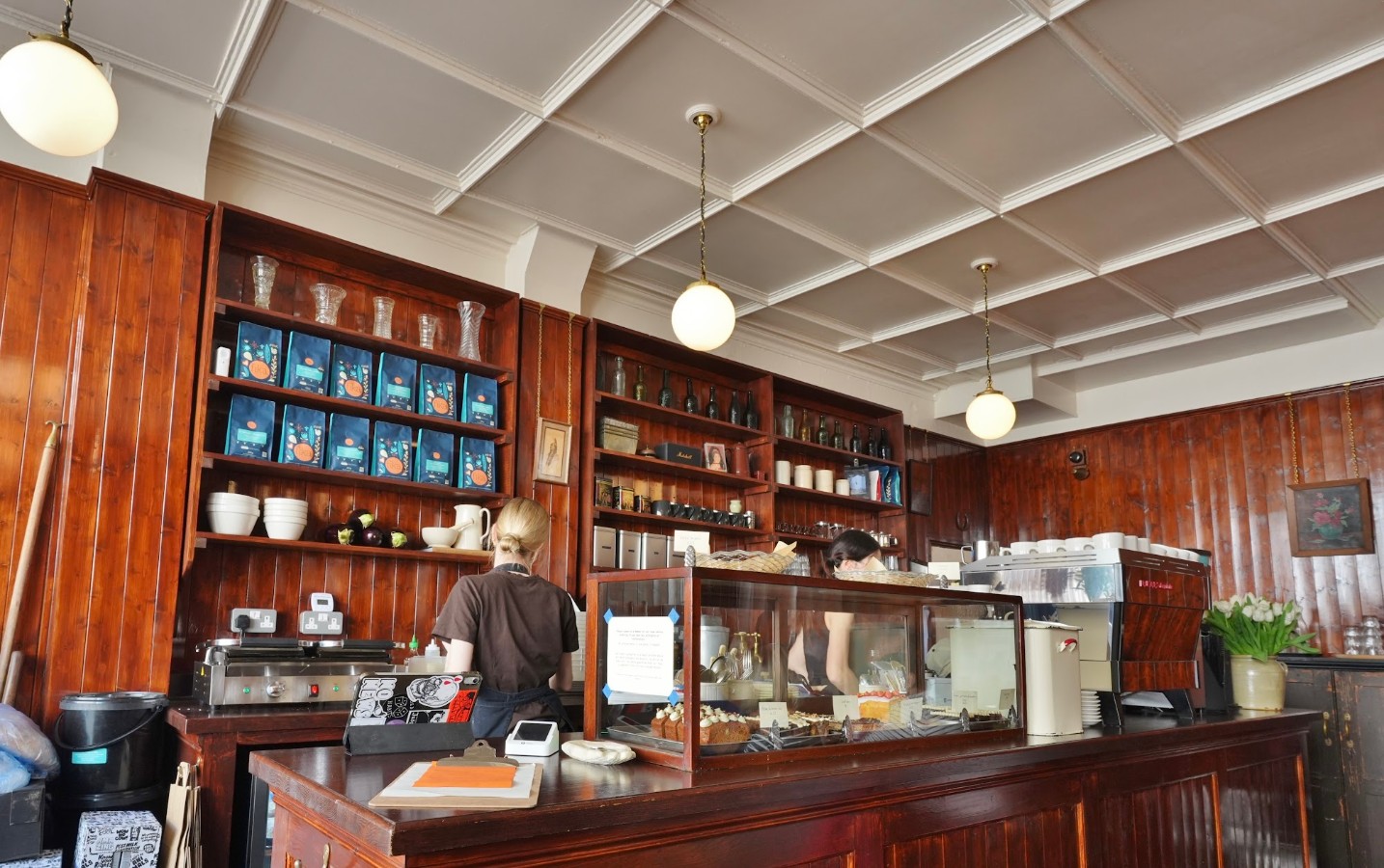Behind the counter: the cake cabinet, the waffle iron, tulips beside the espresso machine.