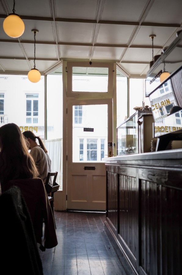The door from inside: lamplight, café curtains, and the CLOSED sign waiting to be flipped.