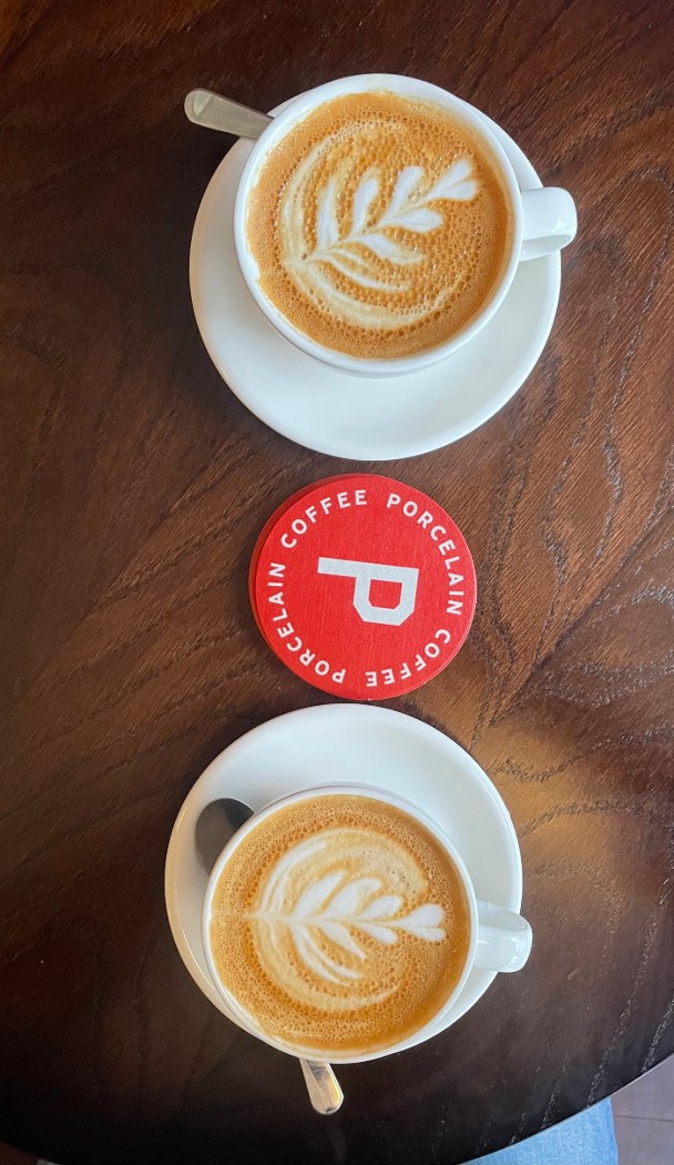 Two flat whites in white porcelain cups either side of the red Porcelain coaster.
